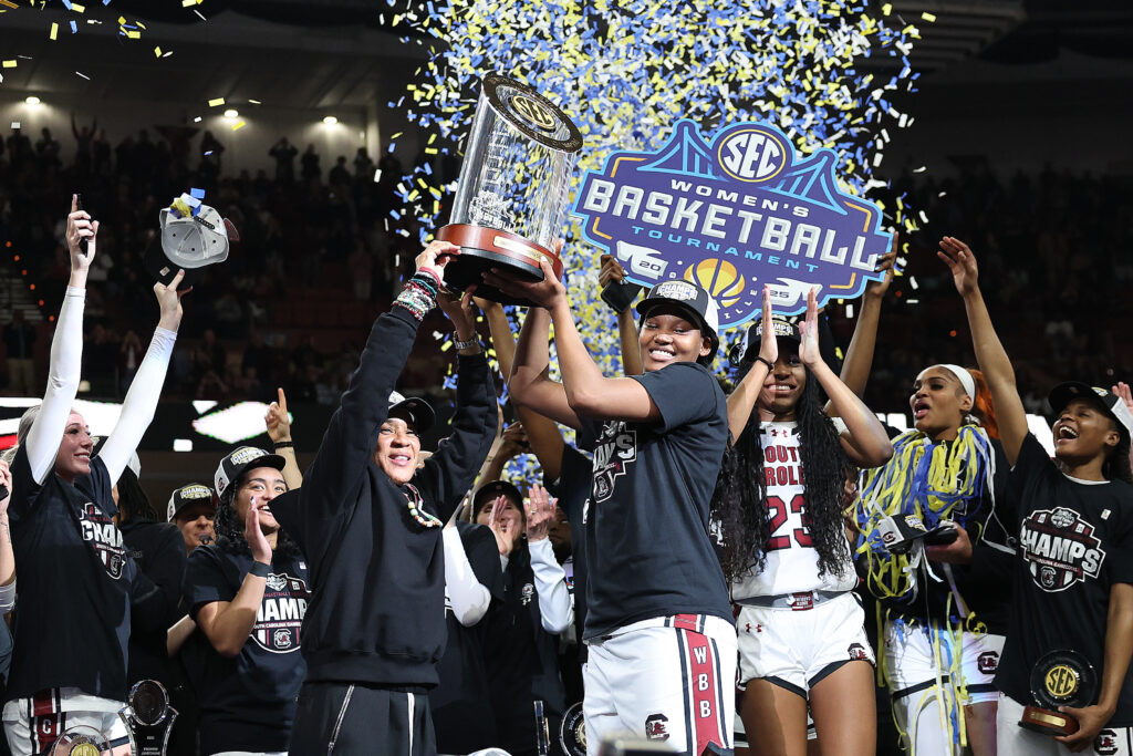 South Carolina basketball head coach Dawn Staley and forward Sania Feagin lift the 2025 SEC tournament trophy as the team cheers.