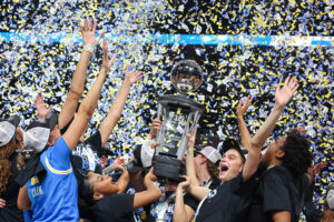 UCLA basketball celebrates and lifts their 2025 Big Ten tournament trophy as confetti falls.