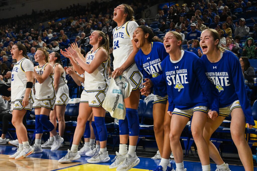 The South Dakota State basketball bench cheers during a 2025 NCAA game.