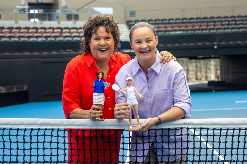 Indigenous Australian tennis stars Evonne Goolagong Cawley and Ash Barty pose at a tennis net with holding their Barbie dolls.