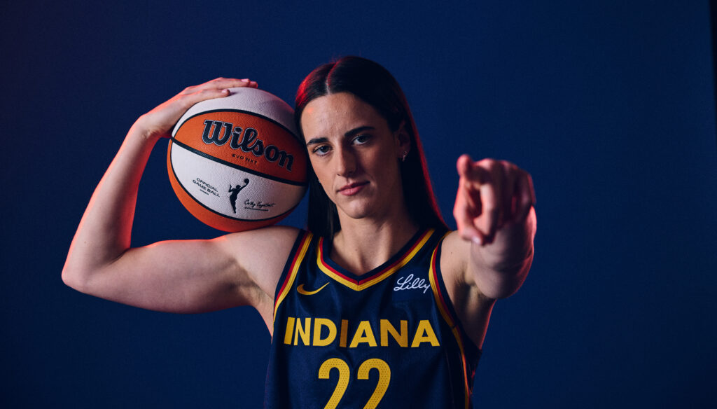Indiana Fever star Caitlin Clark points to the camera holding a basketball during a 2025 WNBA media shoot.