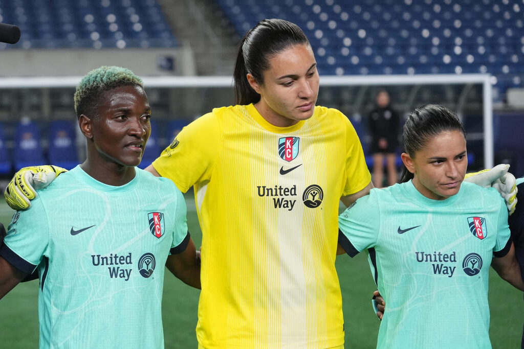 Temwa Chawinga, Lorena, and Debinha stand in a Kansas City Current huddle after a 2025 NWSL match.