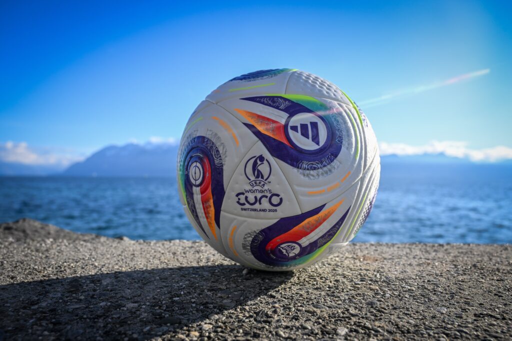 An official 2025 UEFA Women's Euro soccer ball rests on the ground in front of a lake in Switzerland.