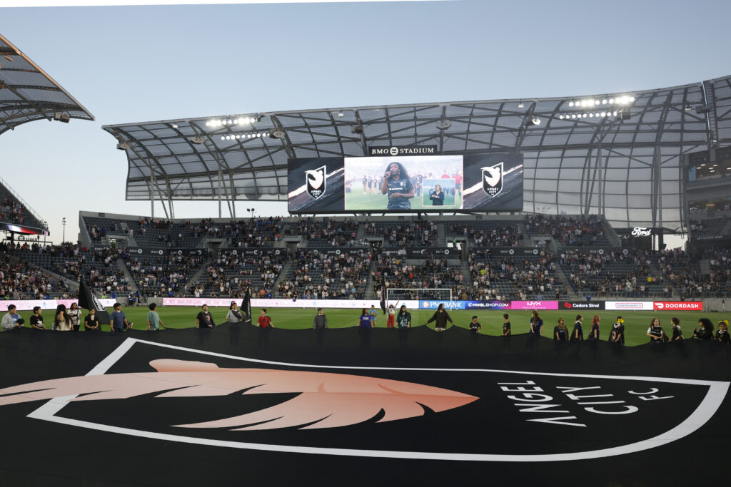 A giant Angel City FC flag is held over the pitch before a 2025 NWSL match.