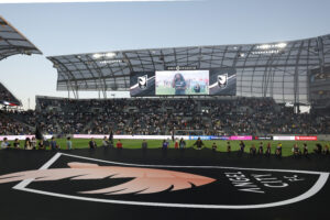 A giant Angel City FC flag is held over the pitch before a 2025 NWSL match.