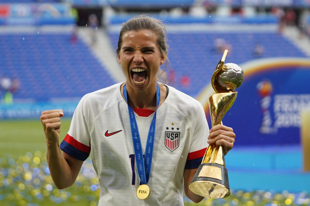 USWNT star Tobin Heath triumphantly yells while holding the 2019 World Cup after winning the final.