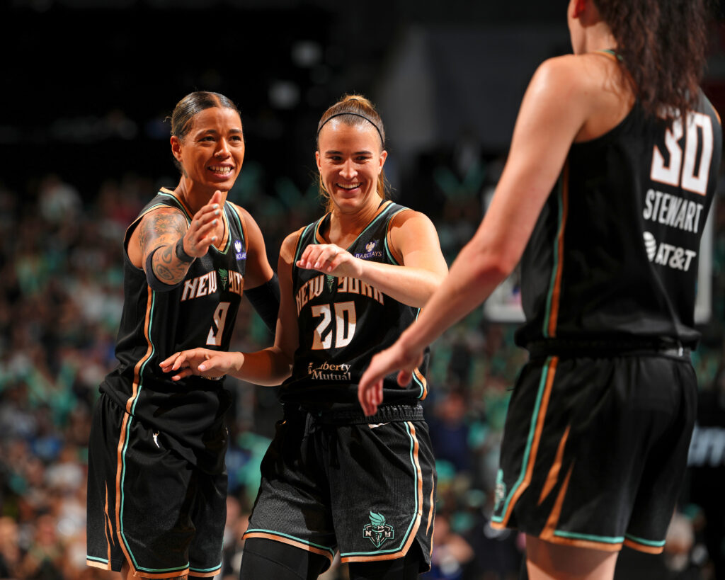 New York Liberty stars Natasha Cloud and Sabrina Ionescu celebrate with teammate Breanna Stewart during a 2025 WNBA game.