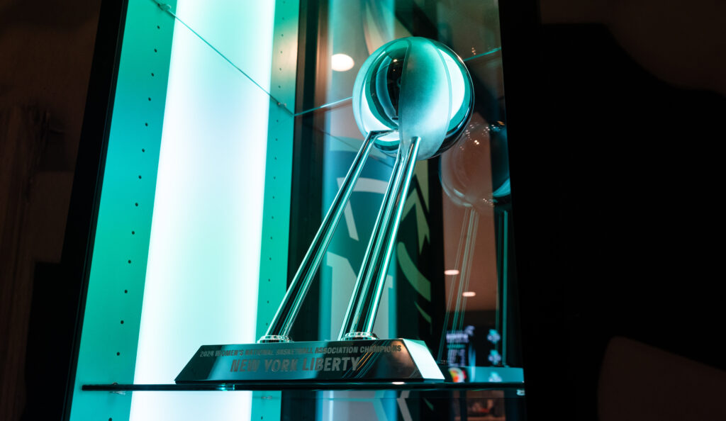 The 2024 WNBA Championship Trophy sits bathed in the New York Liberty's signature seafoam green light.