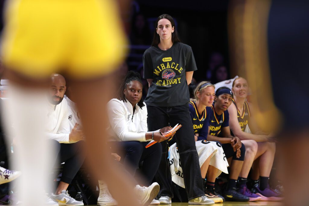Injured Indiana Fever star Caitlin Clark stands in front of the bench during a 2025 WNBA game.