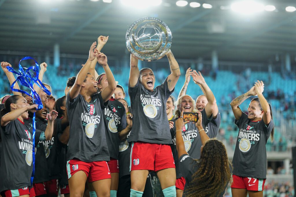 Kansas City forward Bia Zaneratto lifts the 2025 NWSL Shield as her Current teammates cheer.
