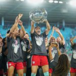 Kansas City forward Bia Zaneratto lifts the 2025 NWSL Shield as her Current teammates cheer.