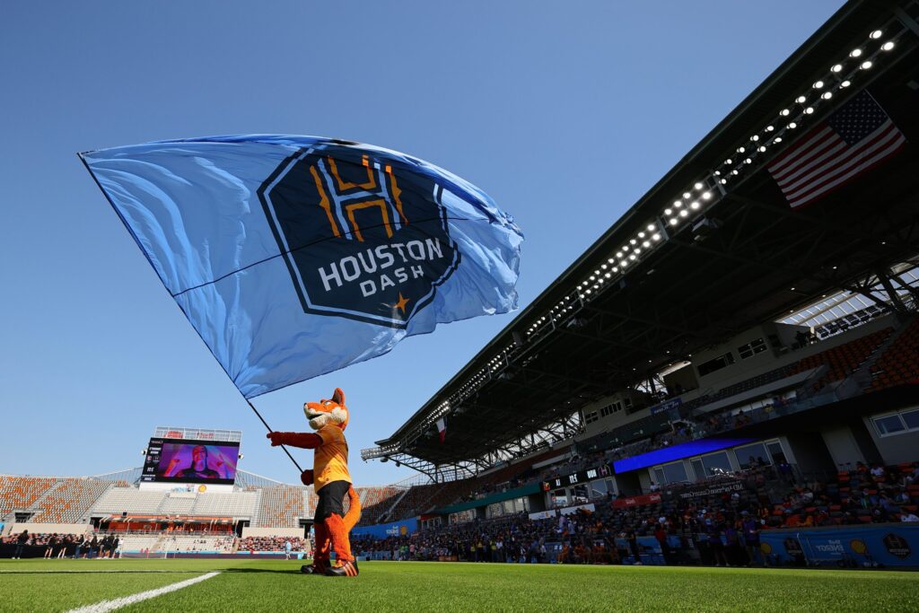 Houston Dash mascot Dynamo Diesel waves a team flag before a 2025 NWSL match.