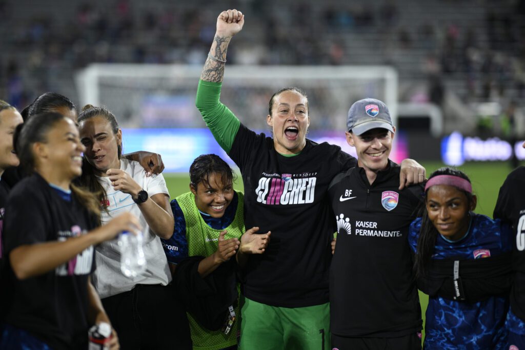 Goalkeeper Kailen Sheridan raises her arm in triumph in a San Diego Wave huddle after a 2025 NWSL match.