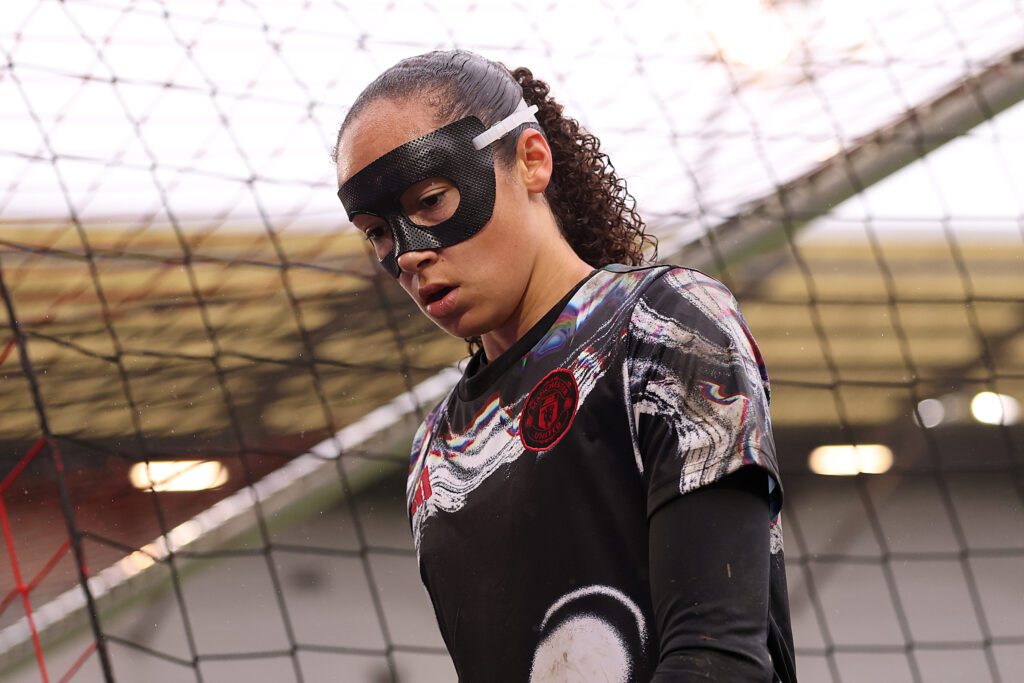 Manchester United goalkeeper Phallon Tullis-Joyce looks down wearing a protective eye mask before a 2025 WSL match.