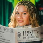 Forward Trinity Rodman looks up over a newspaper whose headline reads "Trinity is staying in DC."