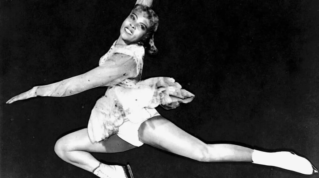 Legendary Black figure skater Mabel Fairbanks jumps in white ice skates against a black backdrop.