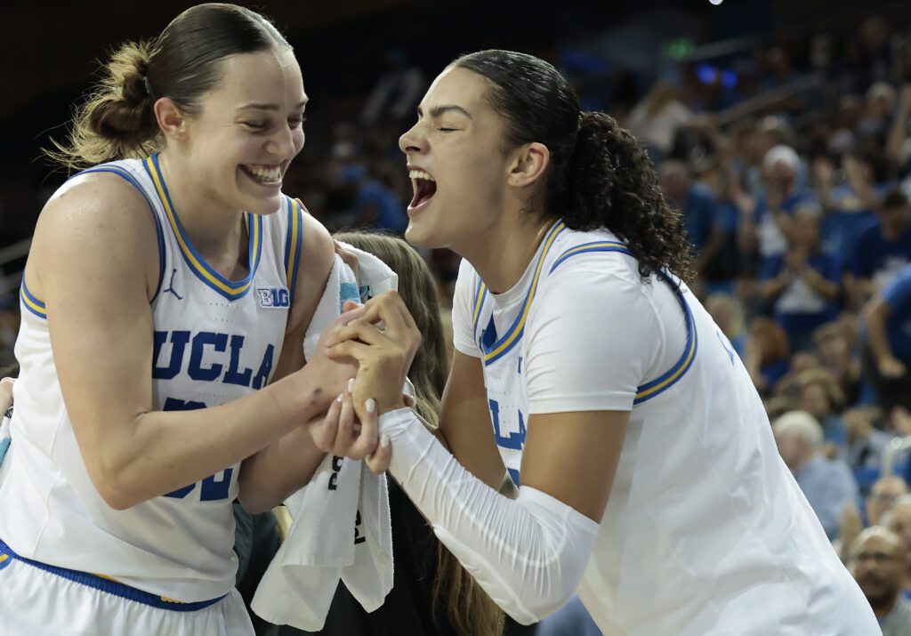 UCLA basketball stars Angela Dugalić and Lauren Betts grin and yell in reaction to a play during a 2025/26 NCAA game.
