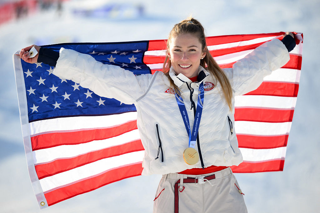 USA's gold medalist Mikaela Shiffrin celebrates with her national flag during the podium ceremony of the women's slalom event during the Milano Cortina 2026 Winter Olympic Games at the Tofane Alpine Skiing Centre in Cortina d'Ampezzo on February 18, 2026.