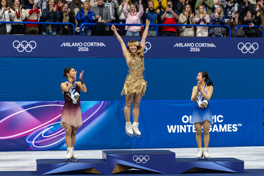 Gold medal winner Alysa Liu of the United States jumps onto the podium to receive her medal watched by silver medal winner Kaori Sakamoto of Japan and bronze medal winner Ami Nakai of Japan during the Figure Skating, Women's Singles Skating, Free Skating at the Milano Ice Skating Arena at the Milano Cortina Winter Olympic Games 2026 on February 19th, 2026 in Milan, Italy.