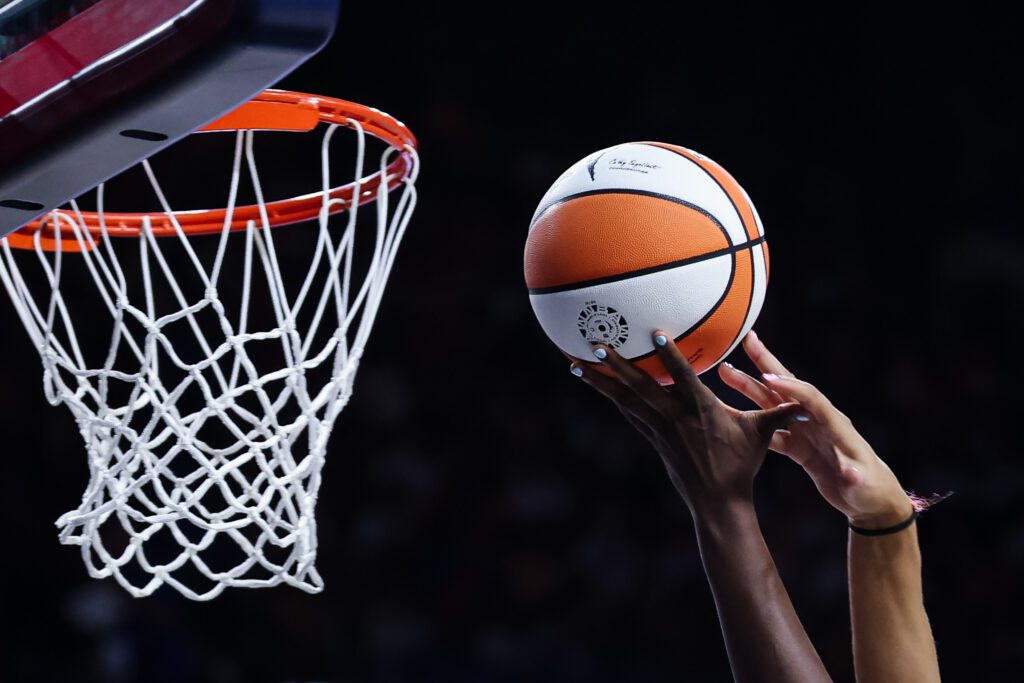 Two players' hands reach for the ball near the basket during a 2025 WNBA game.