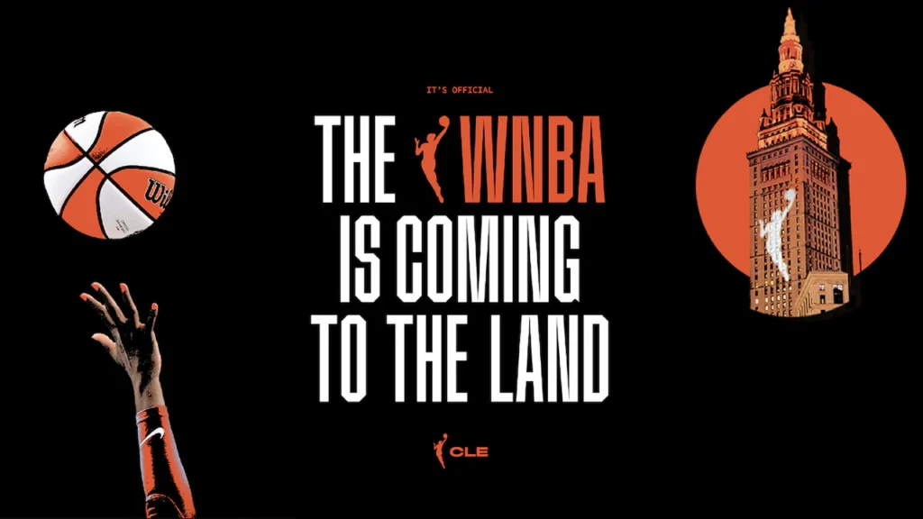 A graphic shows a hand reaching up for a basketball and the WNBA logo projected on Cleveland landmark Tower City while announcing "The WNBA is coming to The Land."
