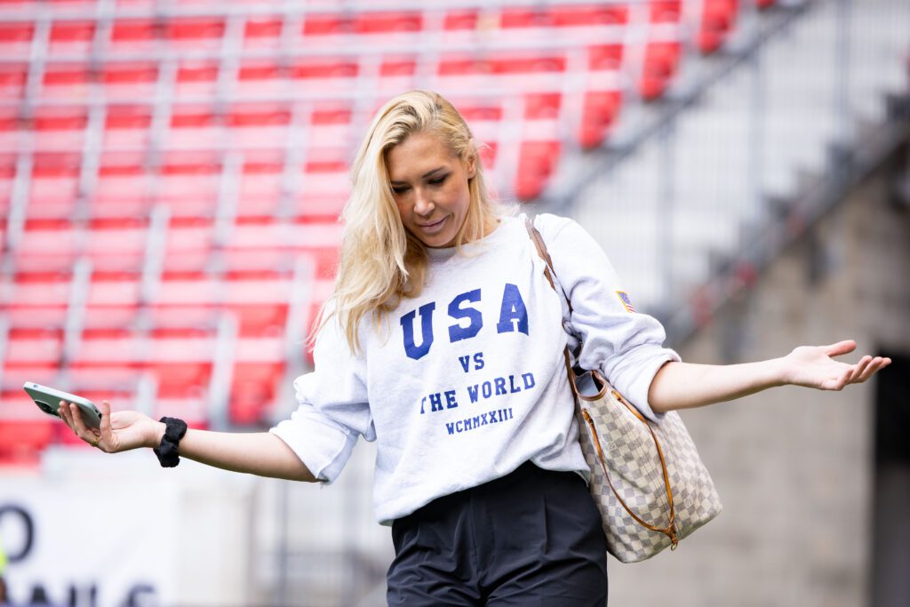 Allie Long #6 of NJ/NY Gotham FC models a sweatshirt that says USA vs The World before the National Womens Soccer League Match against the Chicago Red Stars at Red Bull Arena on June 25, 2023 in Harrison, New Jersey.