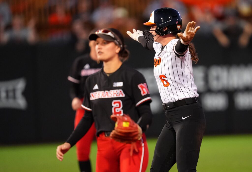 Oklahoma State's Audrey Schneidmiller (6) celebrates a double next to Nebraska's Lauren Camenzind (2) during the college softball game between the Oklahoma State University Cowgirls and the Nebraska Cornhuskers.