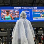 A person in a rain poncho watches the US Open tennis tournament on a screen at the USTA Billie Jean King National Tennis Center in New York on September 1, 2026.