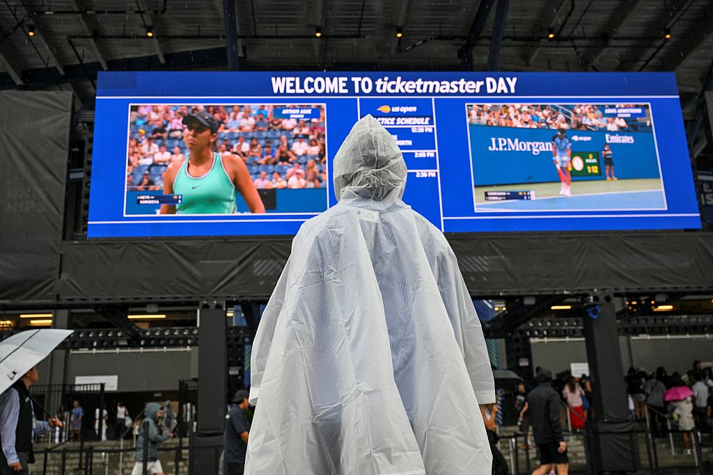 A person in a rain poncho watches the US Open tennis tournament on a screen at the USTA Billie Jean King National Tennis Center in New York on September 1, 2026.
