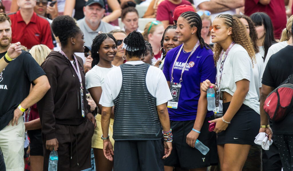 Sep 19, 2026; Columbia, South Carolina, USA; South Carolina Gamecocks women's basketball recruits, from left, GG Banks, Taylor Brown, Jordyn Palmer, and freshman Jerzy Robinson speak with head coach Dawn Staley, back to camera, on the sideline before the football game against the Mississippi State Bulldogs at Williams-Brice Stadium.