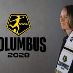 Lucy Rushton poses with a NWSL Columbus 2028 scarf, next to a yellow NWSL logo above "COLUMBUS 2028" text.